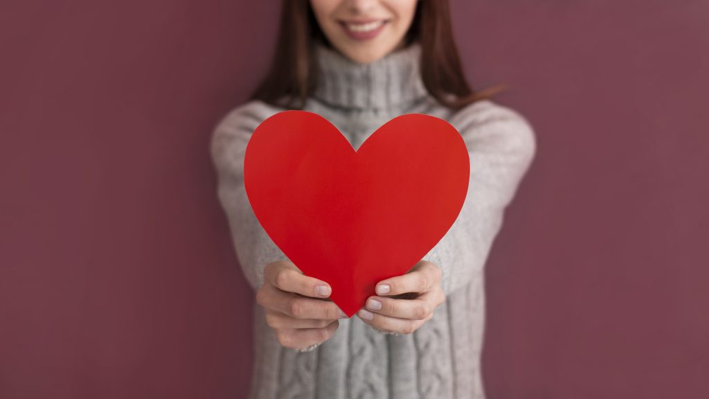 Love concept. Cropped view of smiling girl in sweater, holding heart shaped card isolated