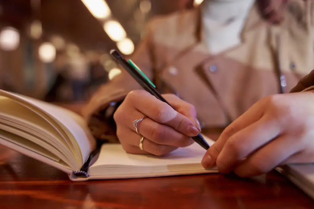 close-up of a woman's hands writing in a self-reflection journal while she waits for her order in a restaurant