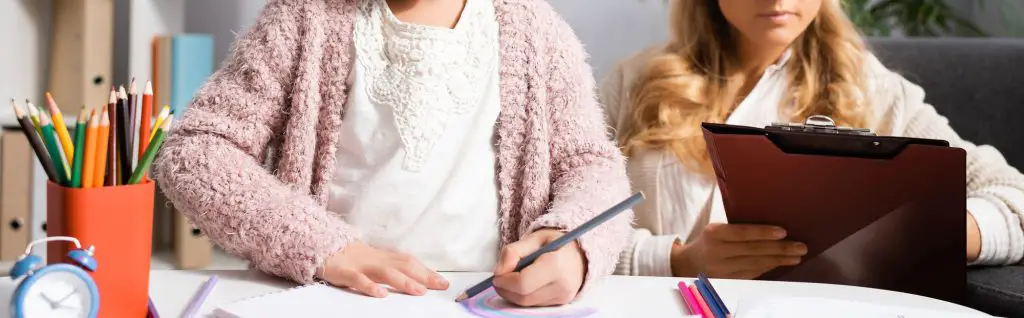 a girl doing art therapy with a therapist who is taking notes