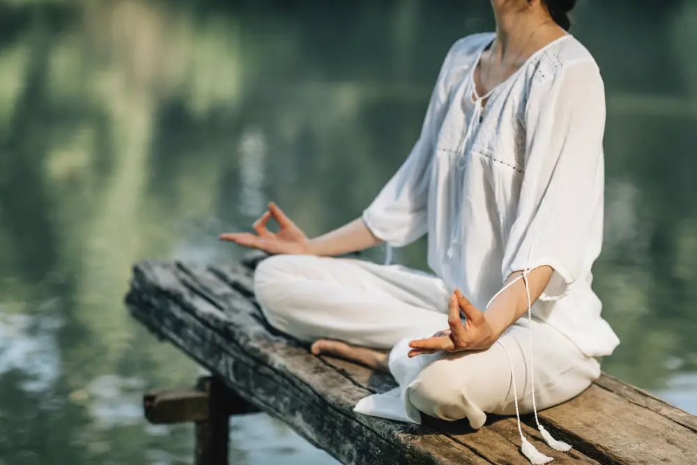 Yoga Retreat. Peaceful young woman sitting in lotus position and meditating by the lake